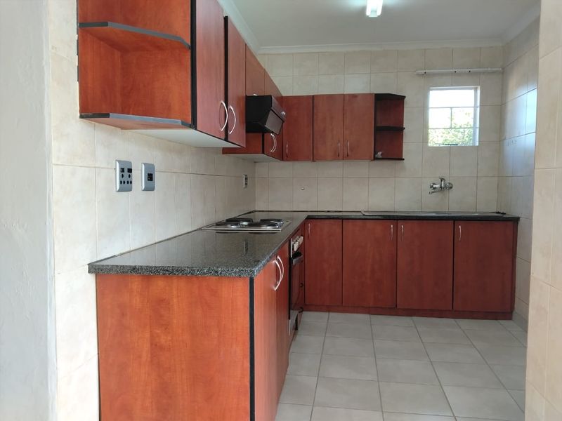 A functional kitchen featuring wood-finish cabinetry, granite countertops, a built-in hob and oven, and tiled finishes throughout.