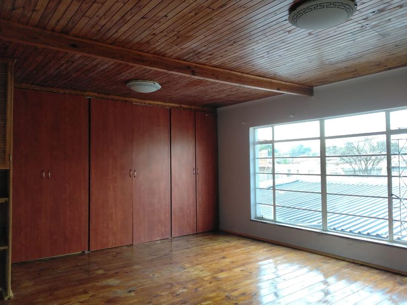 Spacious bedroom featuring timber ceiling, polished timber flooring, and extensive built-in cupboard storage with large windows providing natural light.
