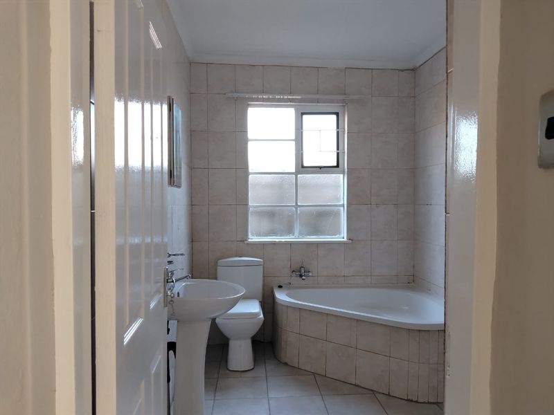 A functional bathroom featuring a corner bathtub, pedestal basin, and toilet with neutral wall and floor tiling.