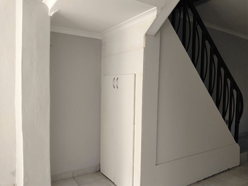 A functional hallway area featuring a built-in storage cupboard, a staircase with a metal balustrade, and tiled flooring.