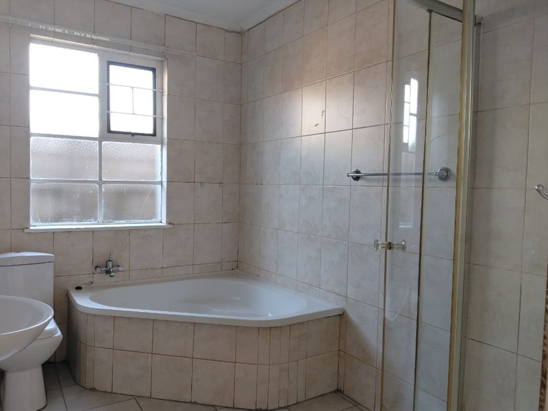 A dated bathroom featuring a corner bathtub, separate glass shower enclosure, pedestal basin, and neutral ceramic tiling throughout.