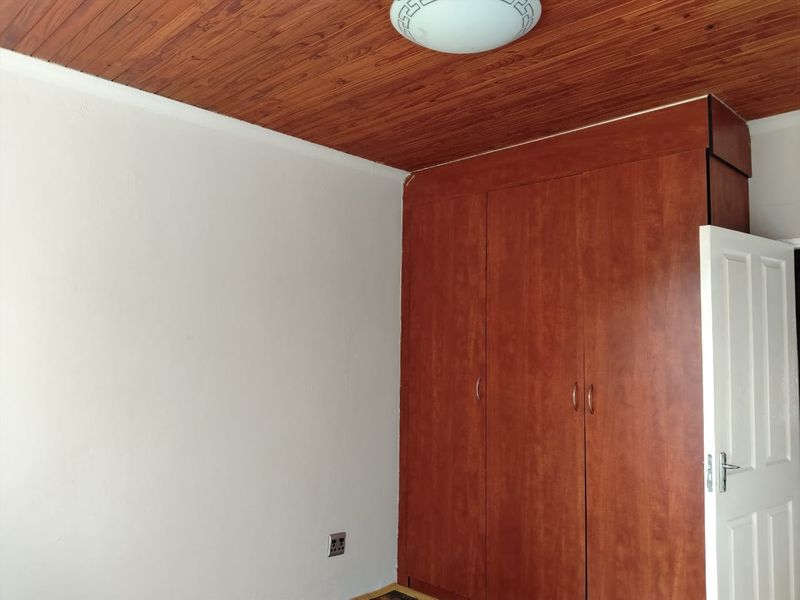 A bedroom featuring a timber-clad ceiling, built-in wooden wardrobe, and a standard panel door, offering a functional space ready for modernization.