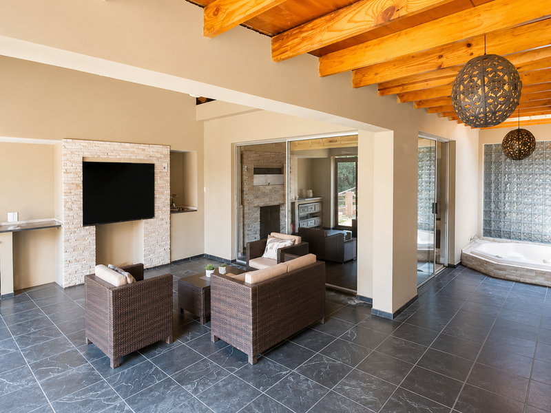 Spacious covered patio featuring exposed timber beams, slate flooring, a stone-clad feature wall, and a built-in corner bathtub with glass block privacy wall.