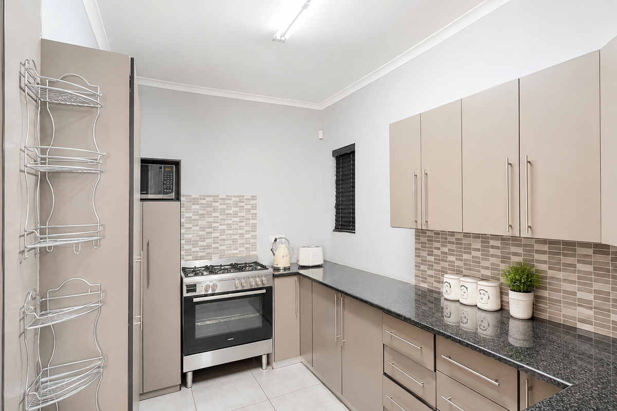 Modern kitchen featuring granite countertops, tiled backsplash, gas stove with oven, and ample built-in cabinetry for storage.