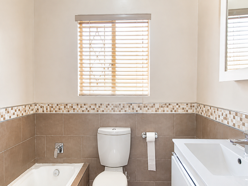 A well-maintained bathroom featuring a built-in bathtub, modern vanity basin, neutral wall tiling with mosaic accents, and a functional medicine cabinet.