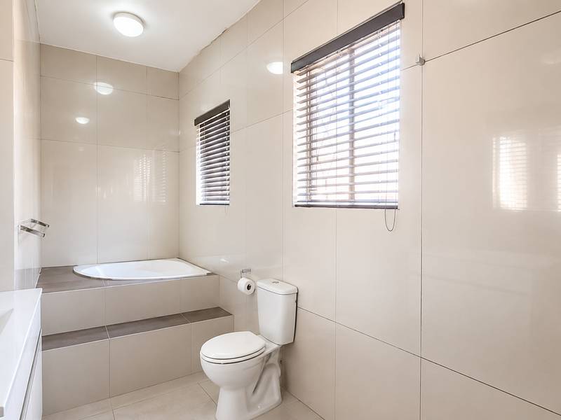 A clean, modern bathroom featuring a built-in bathtub, a white toilet, and a vanity basin with full-height wall tiling.