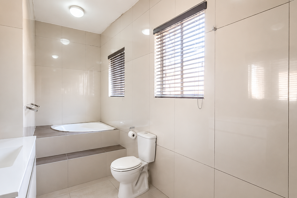 A clean, modern bathroom featuring a built-in bathtub, a white toilet, and a vanity basin with full-height wall tiling.