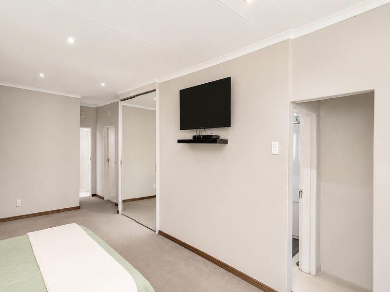 A well-maintained bedroom featuring neutral wall tones, recessed downlights, carpeted flooring, and built-in mirrored sliding wardrobes.