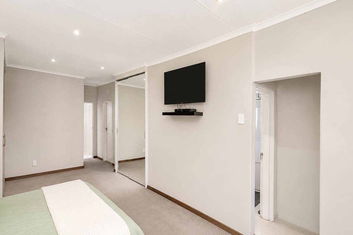 A well-maintained bedroom featuring neutral wall tones, recessed downlights, carpeted flooring, and built-in mirrored sliding wardrobes.
