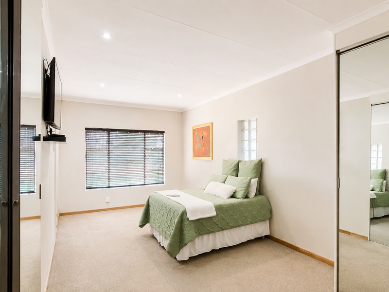 Spacious bedroom featuring neutral walls, carpeted flooring, recessed downlights, and large mirrored sliding wardrobes providing ample storage.