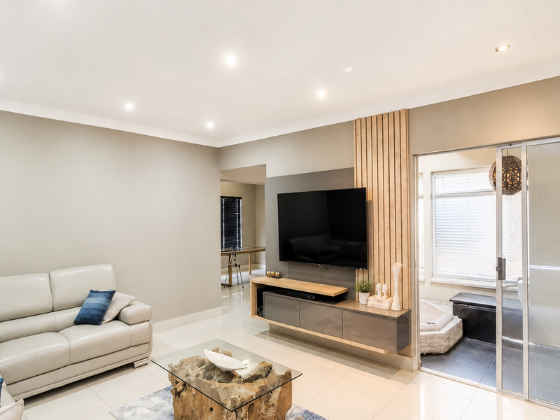 Modern living room featuring a sleek floating media console, decorative slatted timber wall paneling, recessed downlights, and large sliding glass doors leading to an adjacent space.
