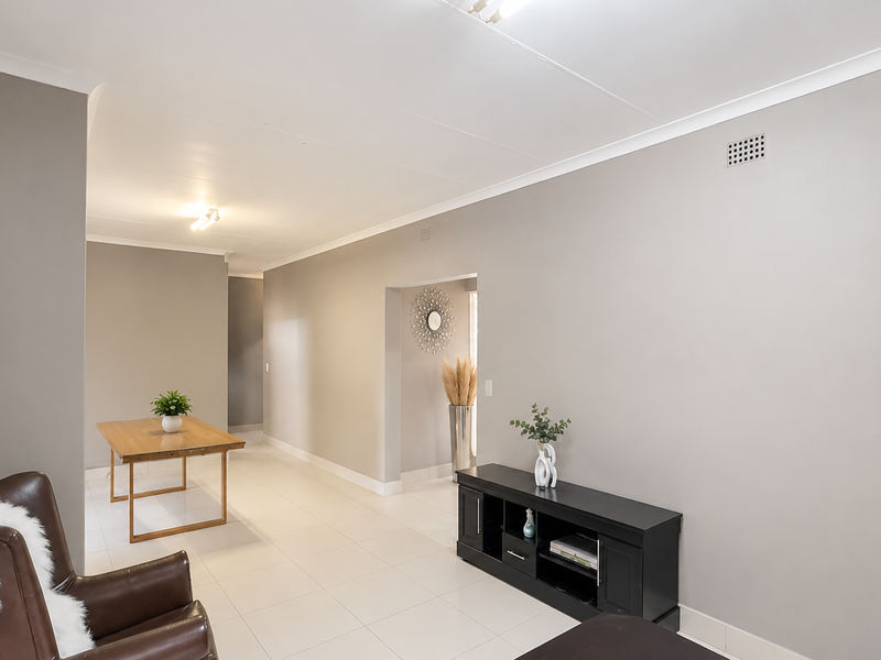 A spacious, neutrally painted living area featuring light-colored floor tiles and clean architectural lines, offering a versatile space for various interior design layouts.