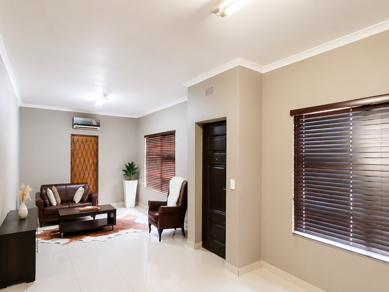 Spacious living room featuring neutral walls, tiled flooring, air conditioning, and large windows with fitted venetian blinds.
