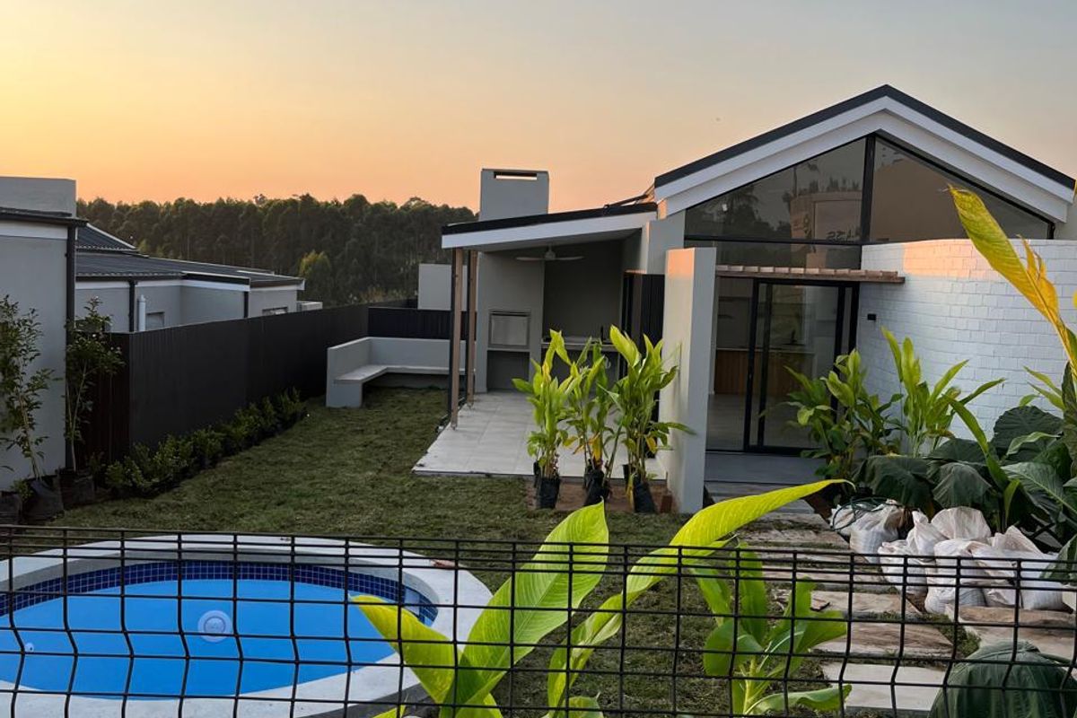 Rear view of a modern home featuring a swimming pool, landscaped garden, and a covered patio area with a built-in braai.