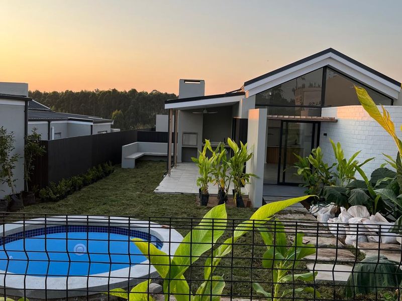 Rear view of a modern home featuring a swimming pool, landscaped garden, and a covered patio area with a built-in braai.