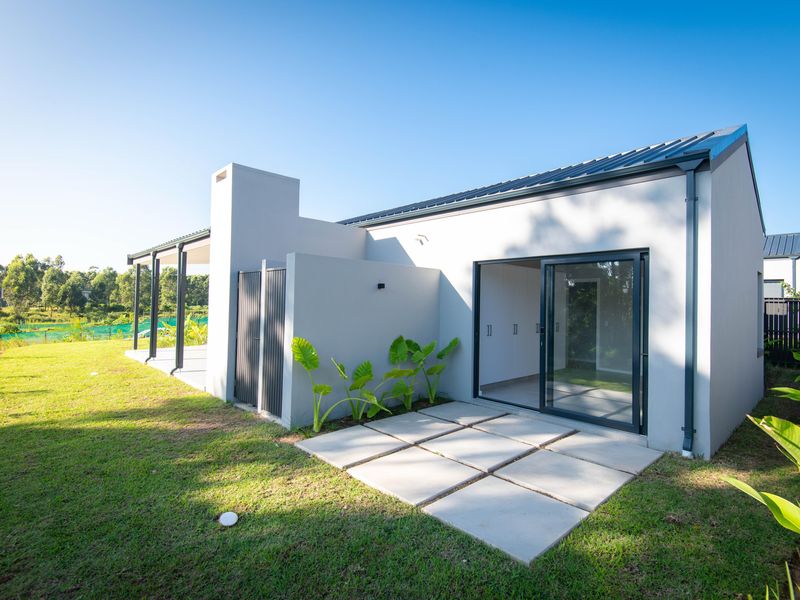 Rear view of a modern house featuring a covered patio, sliding glass doors, and a concrete paver area overlooking the garden.