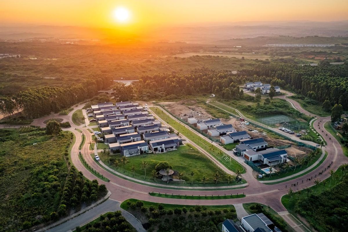 An aerial view of a modern residential estate featuring multiple housing units, paved road networks, and communal recreational facilities at sunset.
