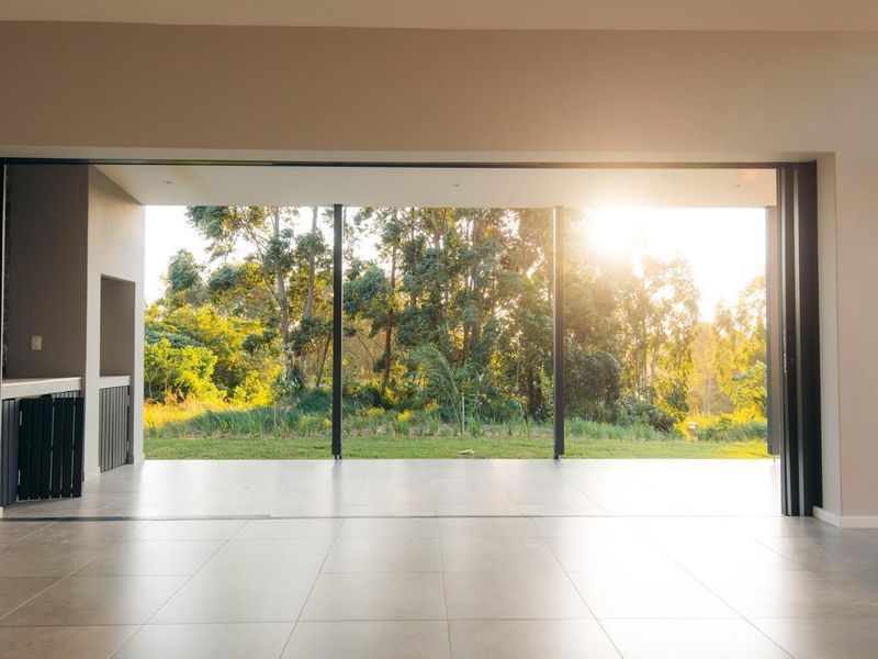 Spacious open-plan living area featuring large format floor tiles and seamless stacking glass doors opening to a scenic garden view.