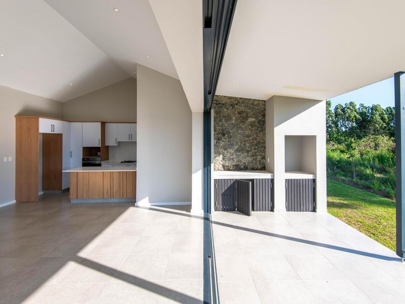 Modern open-plan living area featuring a sleek kitchen with built-in appliances and a seamless transition to a covered patio with a built-in braai.