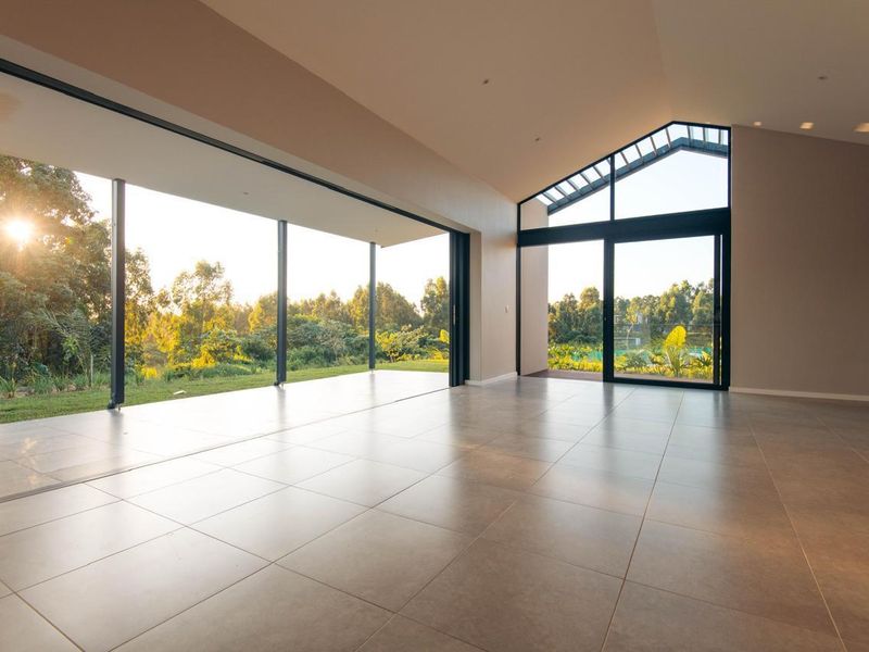 Spacious, light-filled living area featuring large format floor tiles, vaulted ceilings, and expansive sliding glass doors opening to a scenic garden view.