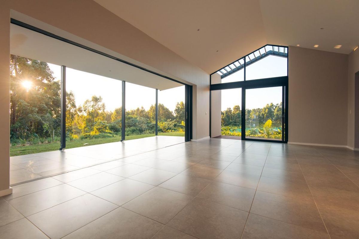 Spacious, light-filled living area featuring large format floor tiles, vaulted ceilings, and expansive sliding glass doors opening to a scenic garden view.