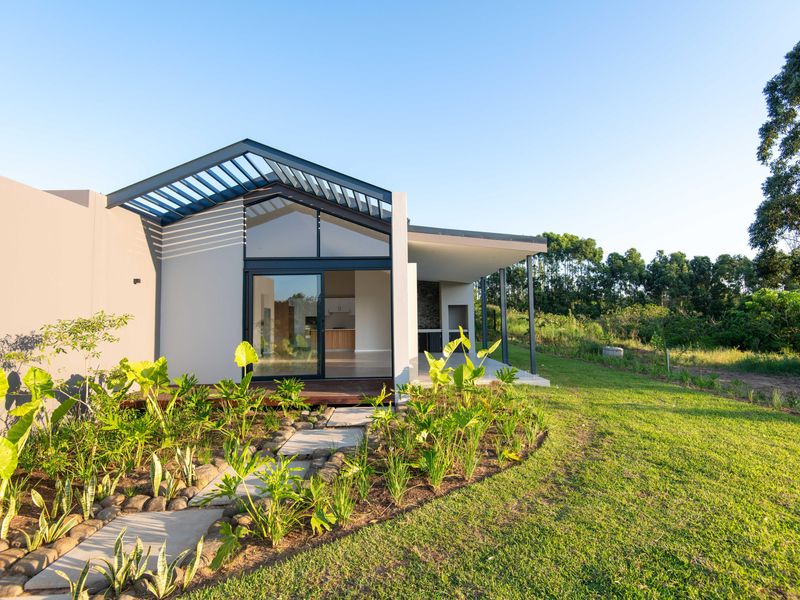 Modern rear exterior featuring a covered patio with built-in braai, timber decking, and a landscaped garden with a stone pathway.