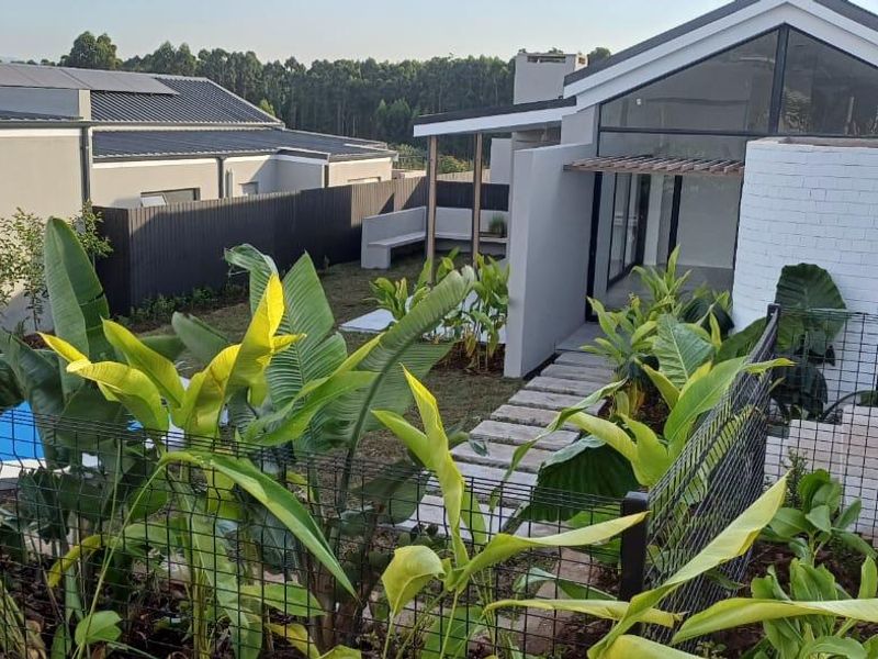 A modern rear exterior view featuring a landscaped garden, swimming pool, stone pathway, and a contemporary home with a pitched roof and pergola.