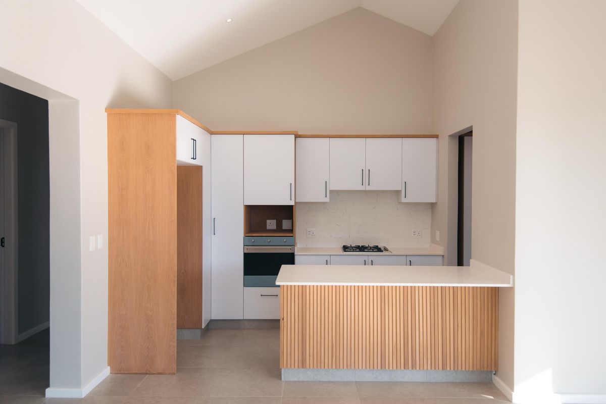 Modern kitchen featuring white cabinetry, wood-paneled island, stone countertops, built-in oven, gas hob, and a high vaulted ceiling.