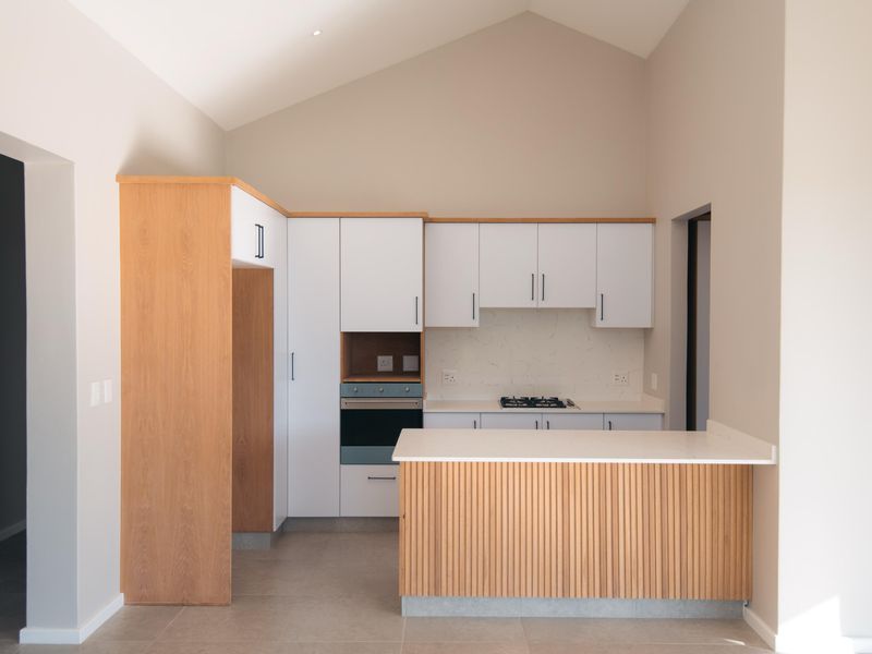 Modern kitchen featuring white cabinetry, wood-paneled island, stone countertops, built-in oven, gas hob, and a high vaulted ceiling.