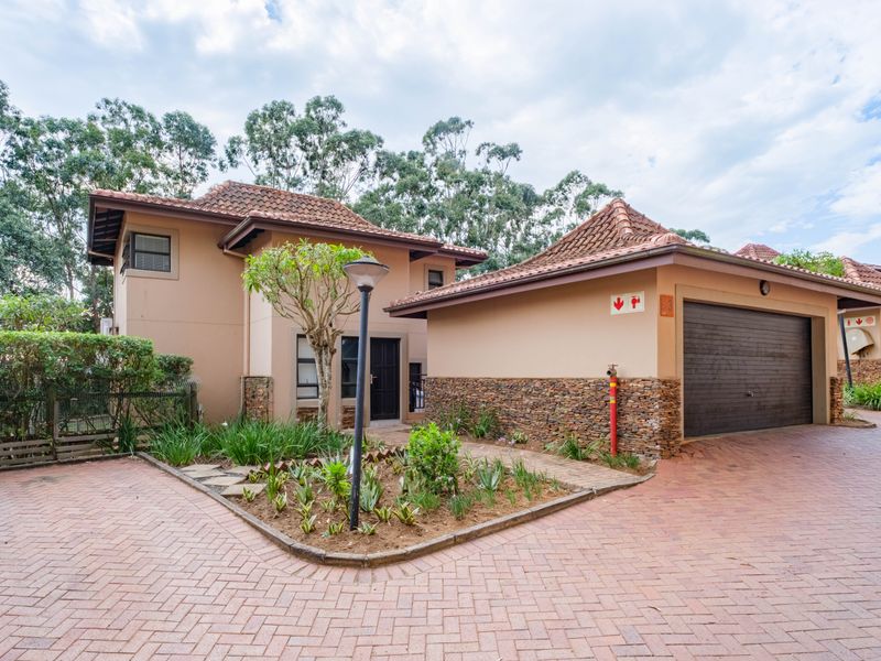 Front elevation of a townhouse featuring a brick paved driveway, stone-clad accents, a tiled roof, and an integrated garage.