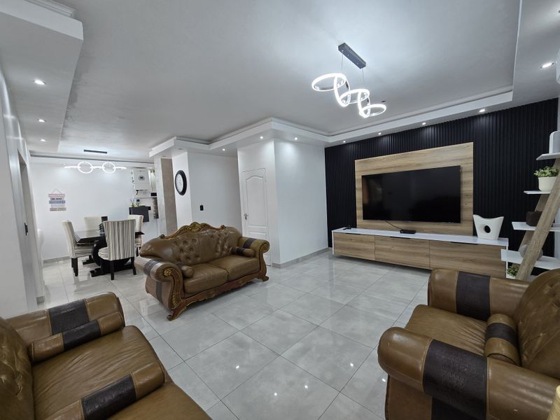 Spacious open-plan living and dining area featuring modern slatted feature wall, built-in media cabinetry, polished porcelain floor tiles, and contemporary recessed and pendant lighting.