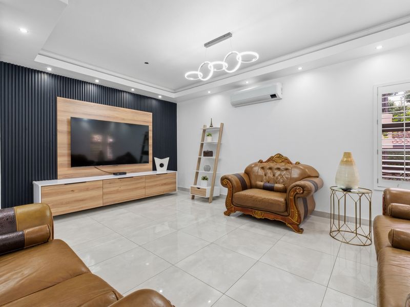A modern living room featuring a slatted feature wall, built-in media console, recessed lighting, and polished porcelain floor tiles.