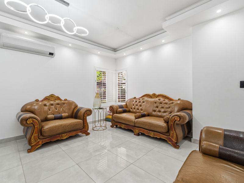 Bright living room featuring polished tiled flooring, recessed ceiling lighting, plantation shutters, and a wall-mounted split-system air conditioner.