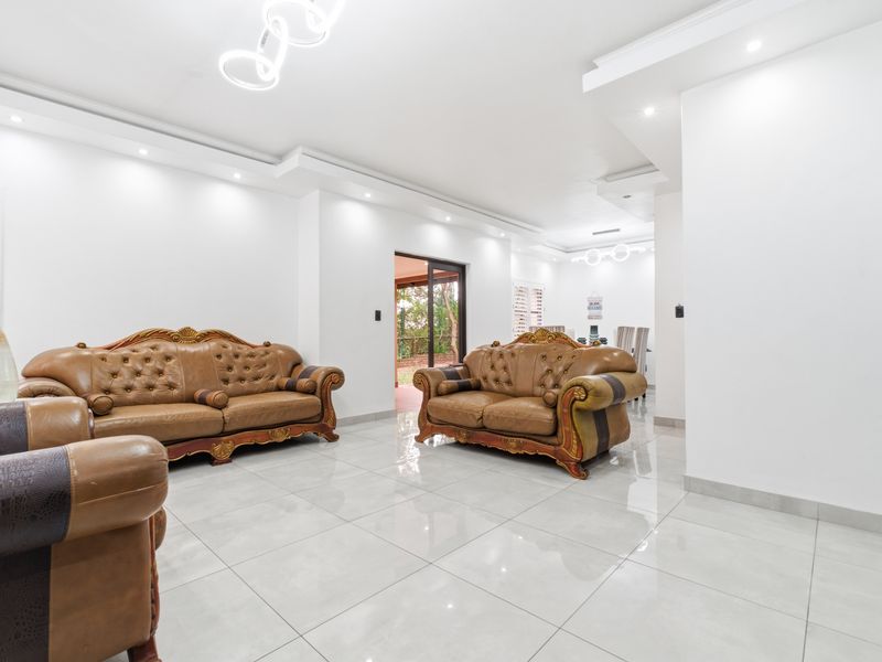 Spacious living room featuring polished porcelain floor tiles, recessed ceiling lighting, and a sliding glass door providing access to the outdoor area.