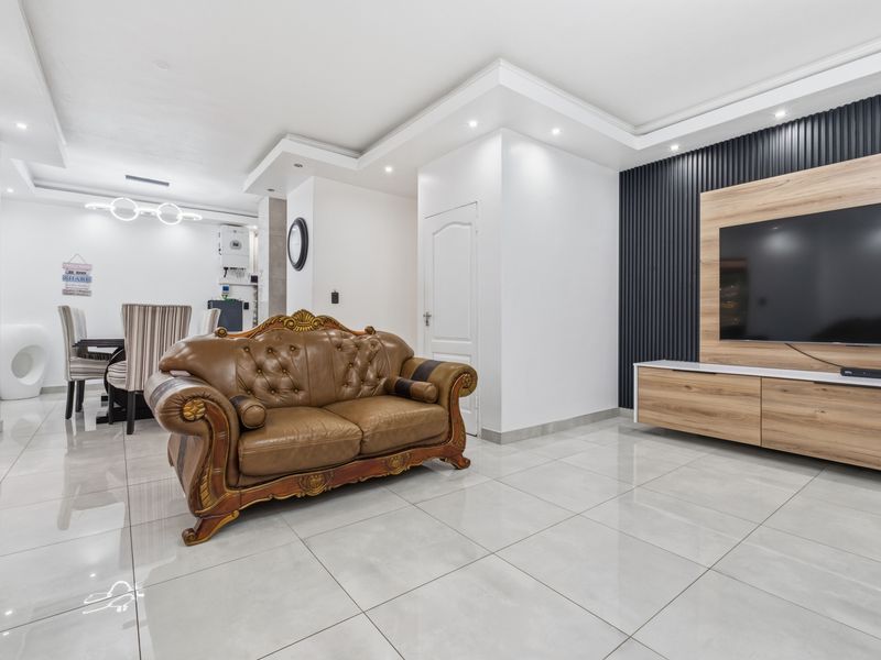Modern open-plan living area featuring polished tile flooring, a contemporary slatted feature wall with built-in media cabinetry, and recessed bulkhead ceiling lighting.