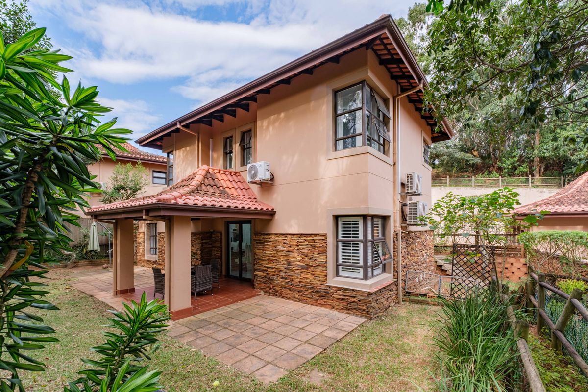 Rear view of the townhouse featuring a covered tiled patio, stone cladding accents, and established garden surroundings.