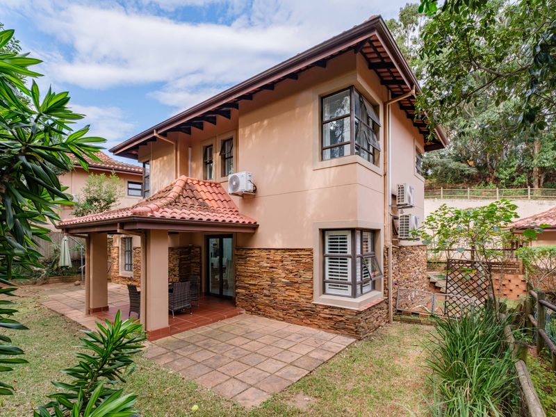 Rear view of the townhouse featuring a covered tiled patio, stone cladding accents, and established garden surroundings.