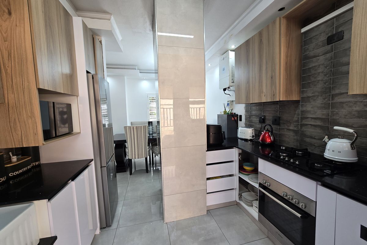 Modern kitchen featuring wood-look and white cabinetry, black stone countertops, gas hob, built-in oven, and tiled finishes, flowing into the adjacent dining area.