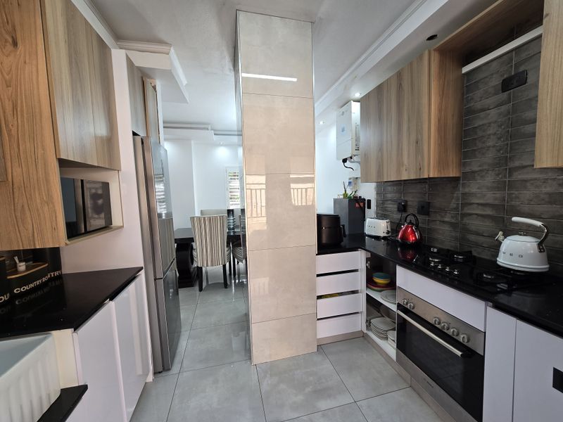 Modern kitchen featuring wood-look and white cabinetry, black stone countertops, gas hob, built-in oven, and tiled finishes, flowing into the adjacent dining area.