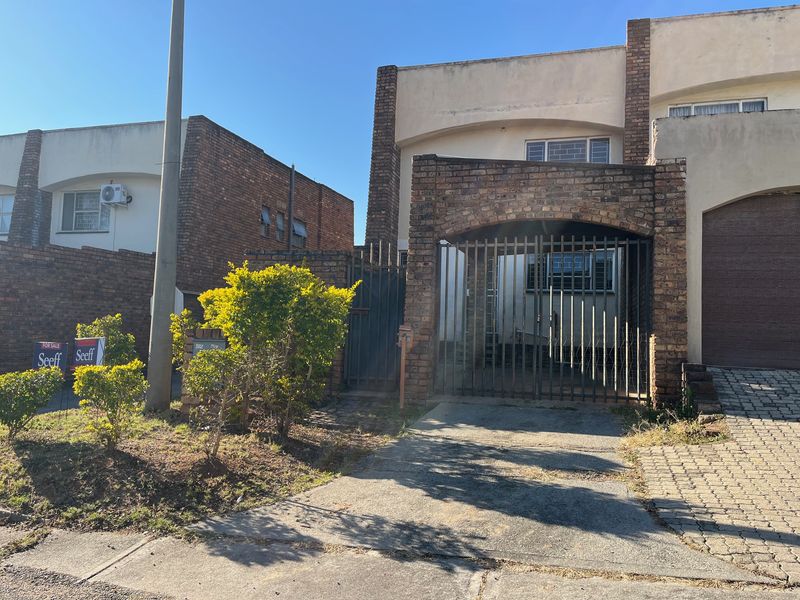 Front elevation of a brick apartment building featuring a gated driveway, security bars on windows, and a paved entrance area.