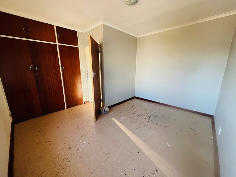 An empty bedroom featuring built-in wooden cupboards, tiled flooring, and neutral walls, requiring cosmetic updates to restore its appeal.