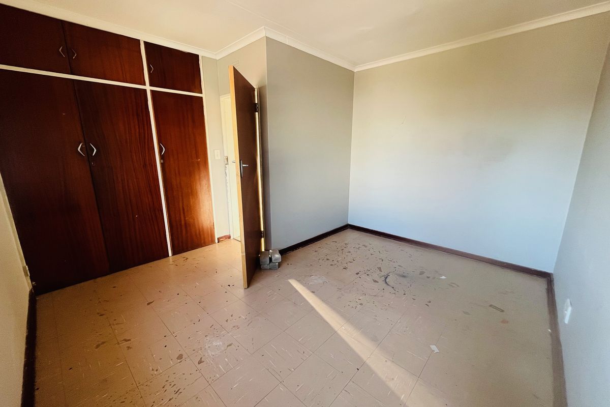 An empty bedroom featuring built-in wooden cupboards, tiled flooring, and neutral walls, requiring cosmetic updates to restore its appeal.