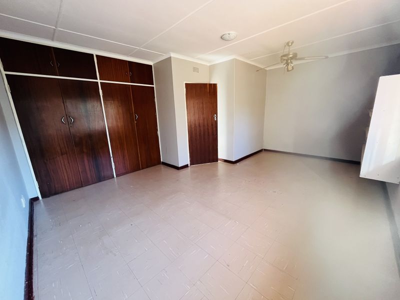 An empty bedroom featuring built-in wooden cupboards, tiled flooring, and a ceiling fan, offering a blank canvas for renovation or restyling.