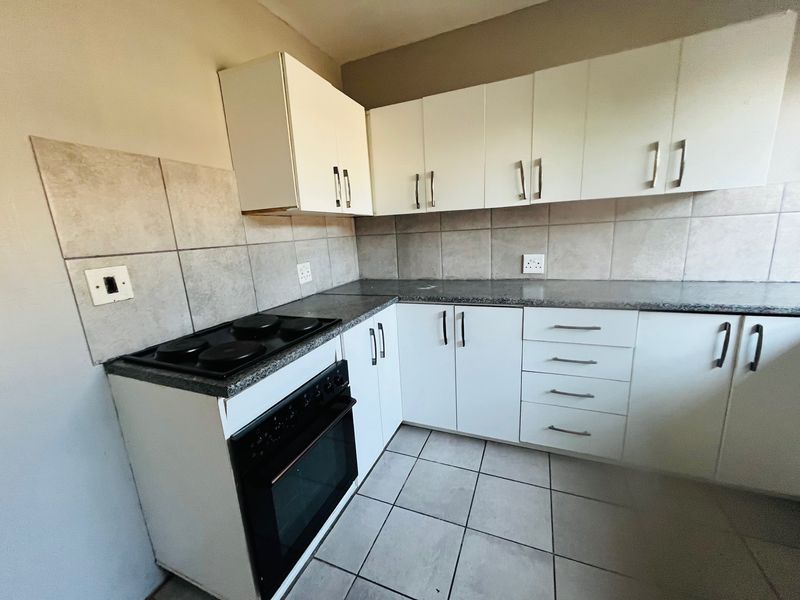 A functional kitchen featuring white cabinetry, granite countertops, a built-in electric stove and oven, and neutral tiled backsplash and flooring.