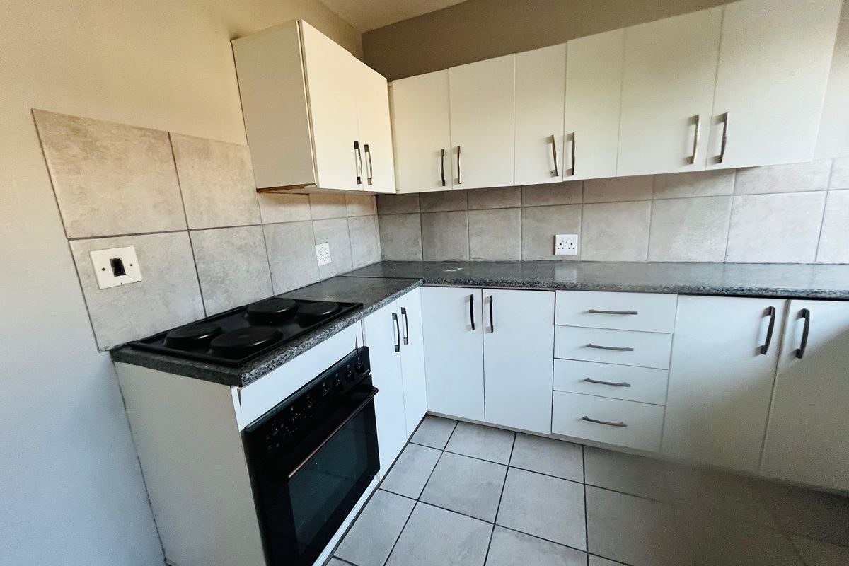 A functional kitchen featuring white cabinetry, granite countertops, a built-in electric stove and oven, and neutral tiled backsplash and flooring.