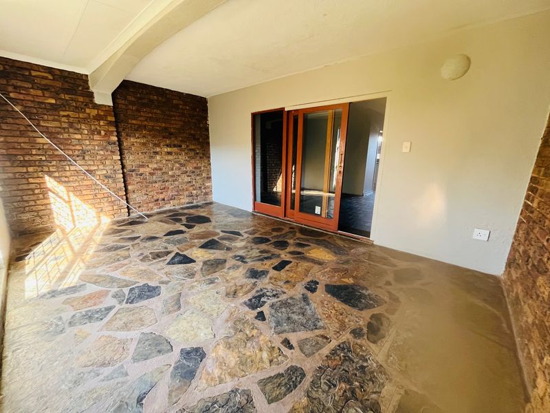 A covered patio area featuring rustic exposed brick walls and distinctive crazy paving stone flooring, accessible via sliding glass doors.