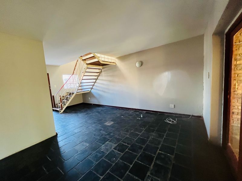 An empty living area featuring dark slate tile flooring and an open-plan staircase leading to the upper level.