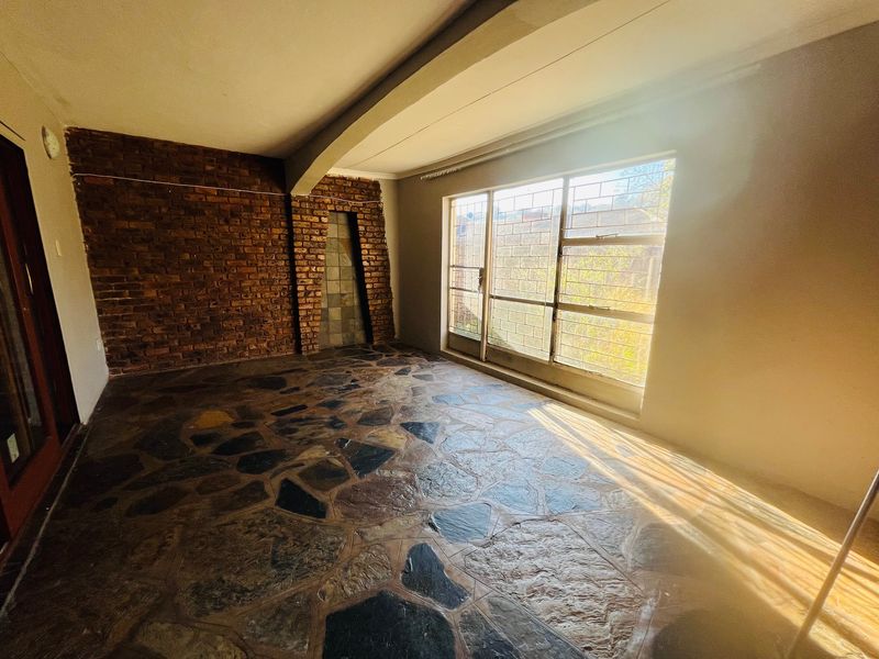 An empty living area featuring a rustic exposed brick wall and unique stone crazy paving flooring, illuminated by natural light from a large window.