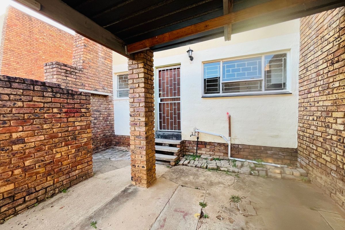 A rear exterior area featuring a covered concrete patio, brick support pillar, and security-fitted door and window access.