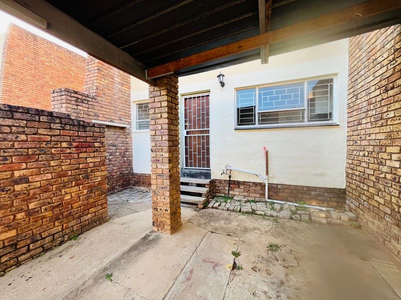 A rear exterior area featuring a covered concrete patio, brick support pillar, and security-fitted door and window access.